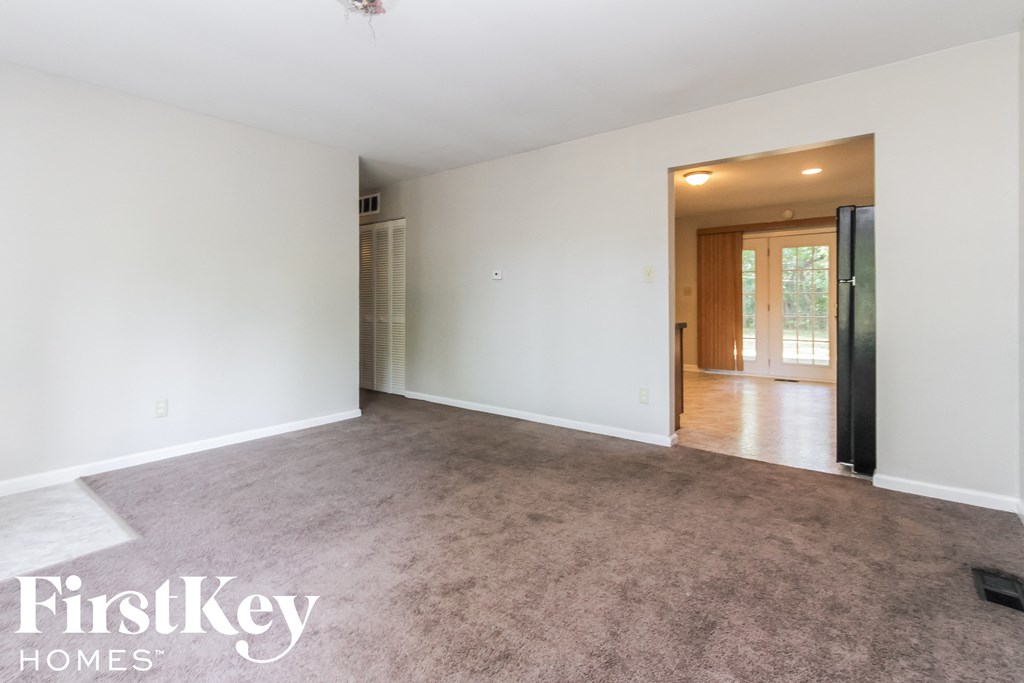 an empty living room with carpet and a door to the kitchen