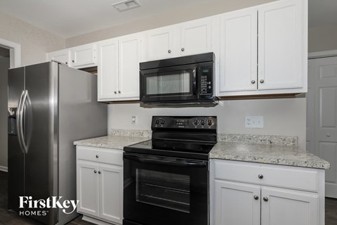 A kitchen with white cabinets and a black microwave above the stove.