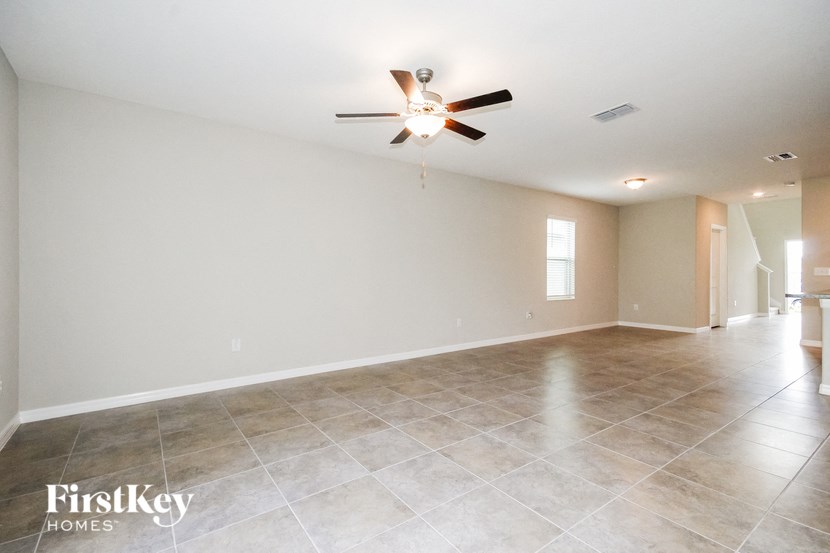 A spacious room with a ceiling fan and light fixture, and a tiled floor.