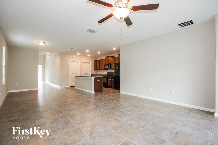 A spacious room with a fan and a kitchen area in the background.