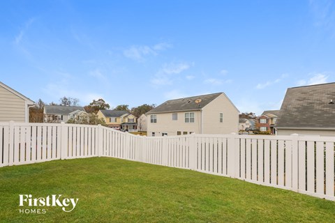 A white picket fence in a grassy area with houses in the background.
