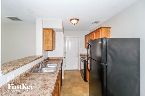 A kitchen with a black fridge and a sink with a brown granite counter top.