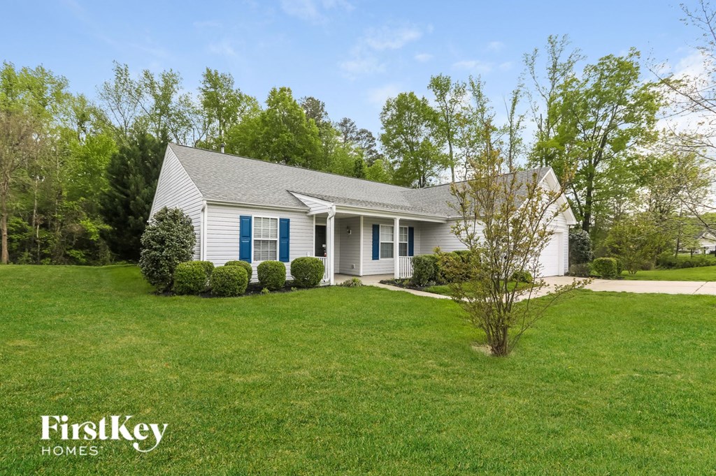A white house with a blue stripe on the front door is surrounded by greenery.