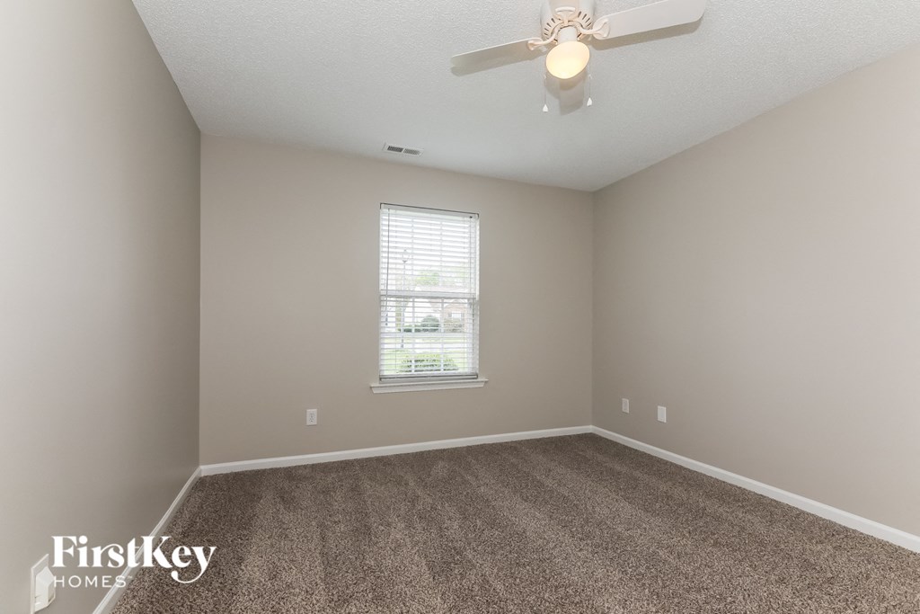 A room with a carpeted floor, a ceiling fan, and a window with blinds.