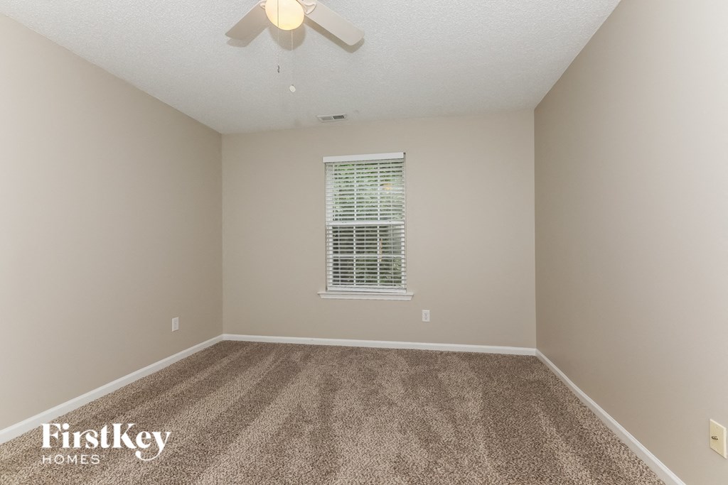 A carpeted room with a ceiling fan and a window with blinds.