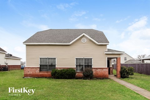 a beige house with a brick porch and a lawn