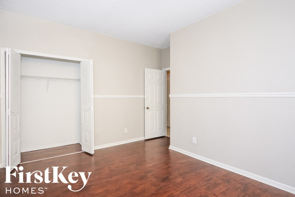a bedroom with white walls and wood floors and a closet