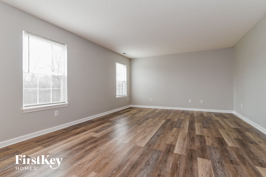 A room with wooden flooring and two windows.