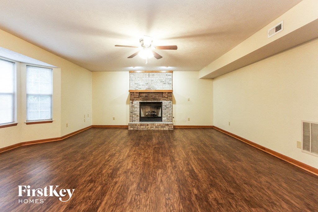 a living room with a fireplace and wooden floors and a ceiling fan