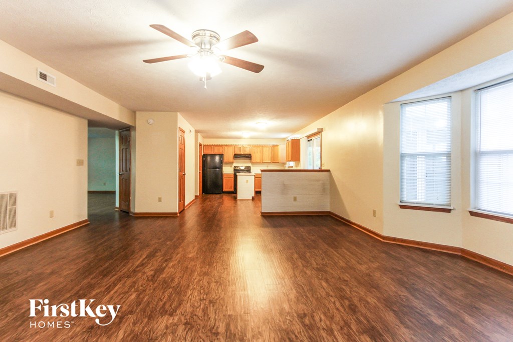 an empty living room with a ceiling fan and a kitchen
