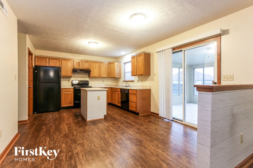 an empty kitchen with wood flooring and a black refrigerator