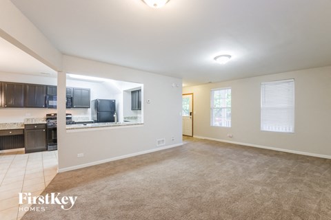 an empty living room with a kitchen in the background