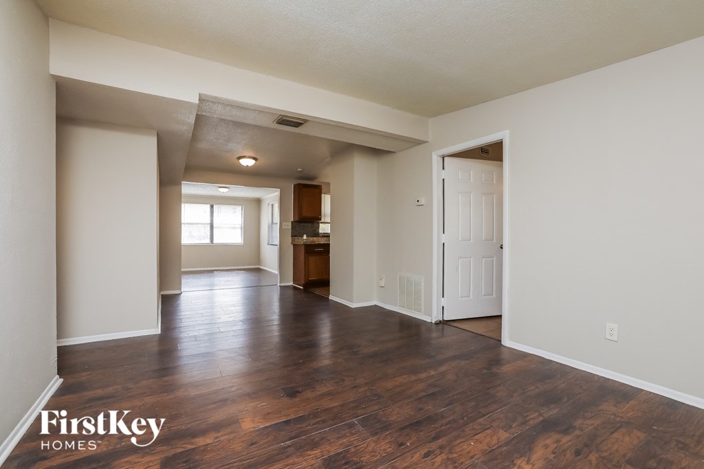 an empty living room and kitchen with hard wood flooring and white walls