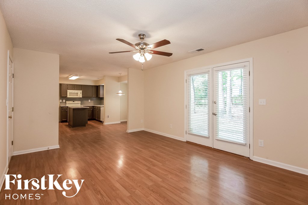an empty living room with a ceiling fan and a kitchen