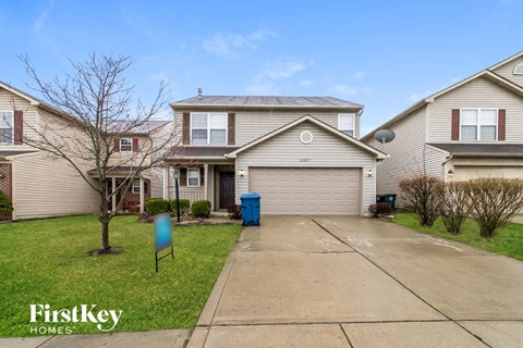 a beige house with a driveway and a blue trash can