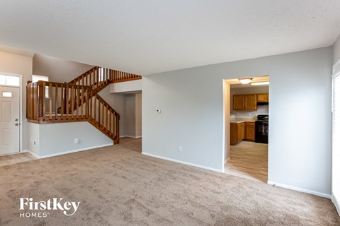 A spacious room with a carpeted floor and a wooden staircase.