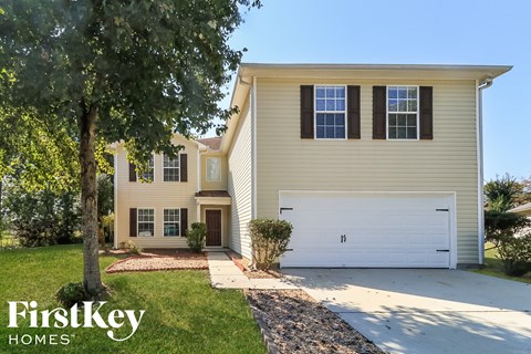 a yellow house with a white garage door and a tree