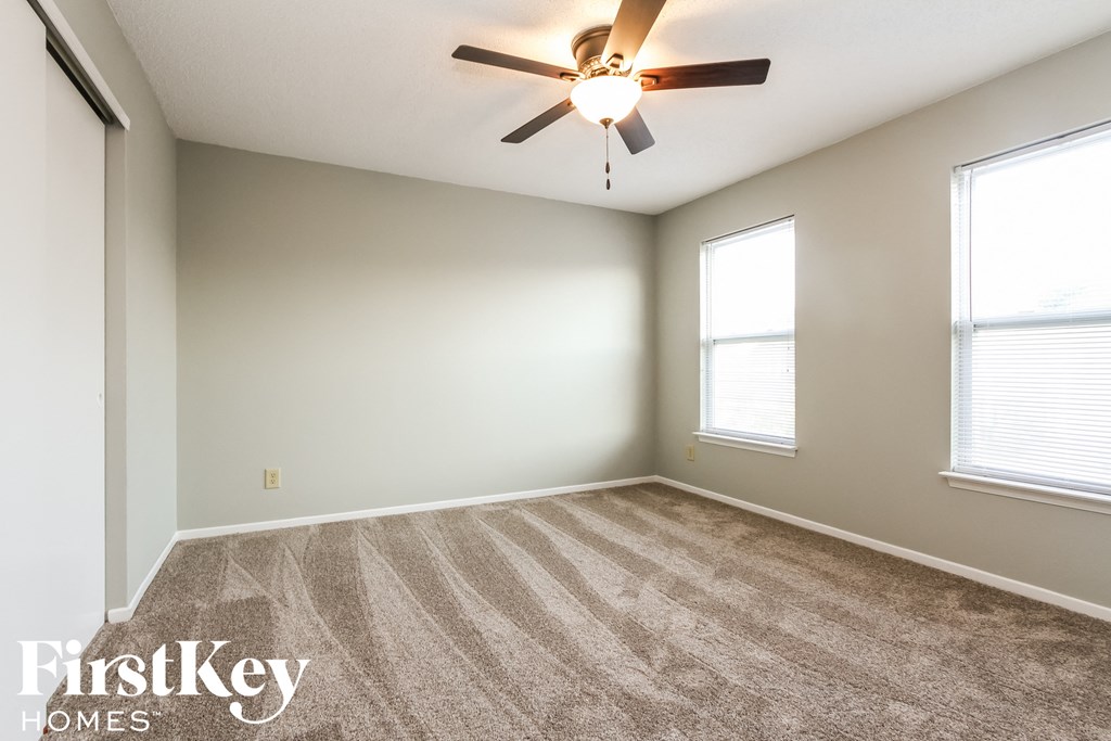 an empty living room with a ceiling fan and two windows