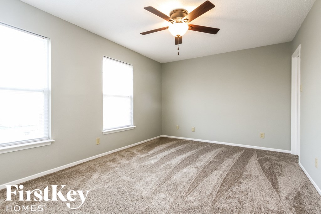 an empty room with a ceiling fan and two windows
