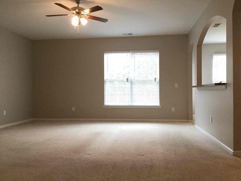 an empty living room with a ceiling fan and a window