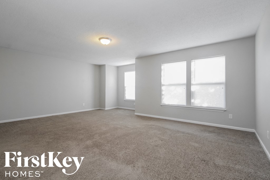 A spacious room with a carpeted floor and two windows.