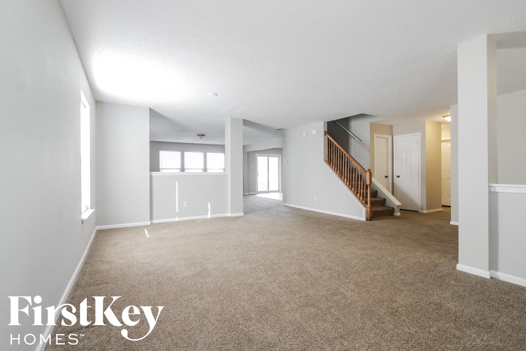 A spacious empty room with a staircase and a window.