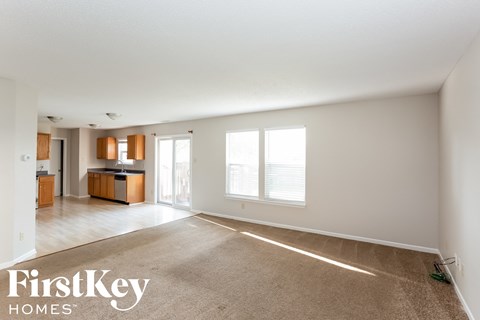A spacious living room with a kitchen in the background and a carpet on the floor.