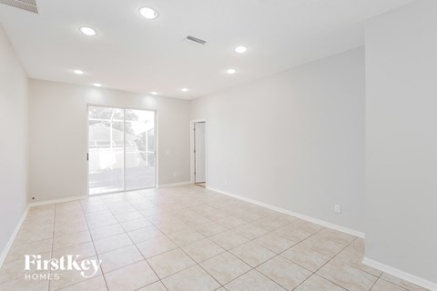 A spacious empty room with tiled flooring and a sliding glass door leading outside.