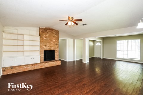 A spacious room with a brick fireplace and wooden floors.