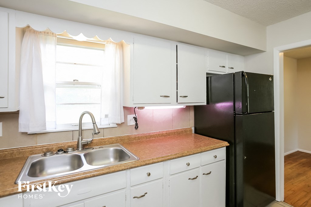 A kitchen with a sink, cabinets, and a refrigerator.