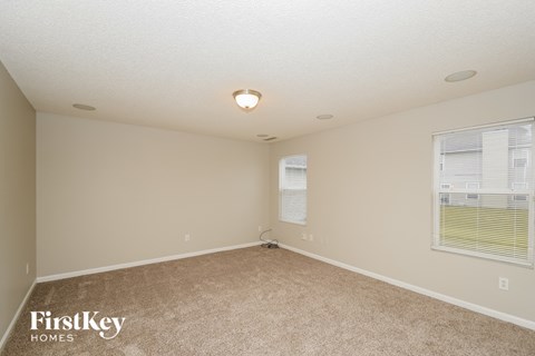 A spacious empty room with a carpeted floor and a window with blinds.