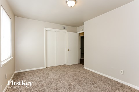 a bedroom with white walls and carpet and a door to a closet