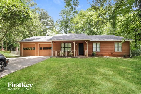 A house with a brown exterior and a grey roof is surrounded by greenery.