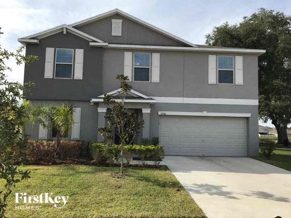 A grey house with a white garage door and a tree in front.
