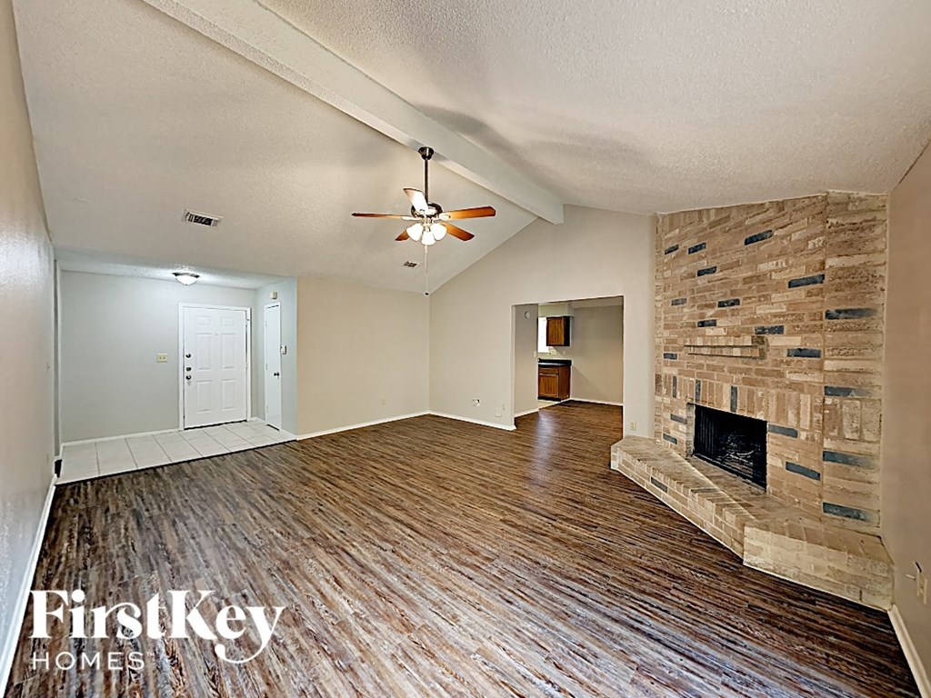 an empty living room with a stone fireplace and wood flooring