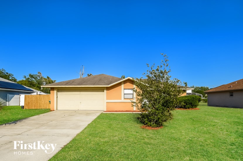 A house with a brown roof and a garage door is surrounded by a green lawn.