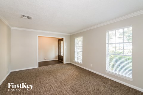 a spacious living room with carpet and a door to a hallway