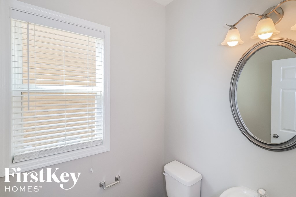 A bathroom with a toilet, a mirror and a window with blinds.