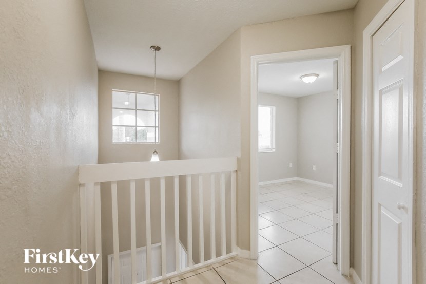 a landing with a white railing and a hallway with a door and a window