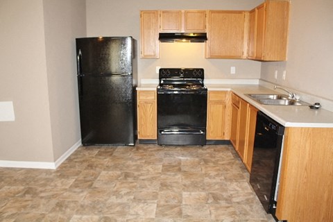 A black refrigerator sits in a kitchen with wooden cabinets and a black stove.