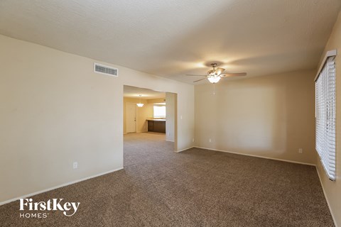 a spacious living room with carpet and a ceiling fan