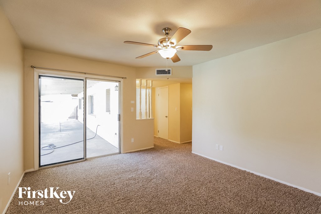 an empty living room with a ceiling fan and a sliding glass door