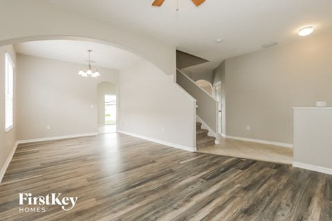 A spacious room with wooden flooring and a staircase in the background.