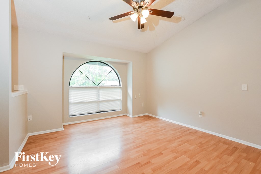 an empty living room with a large window and a ceiling fan