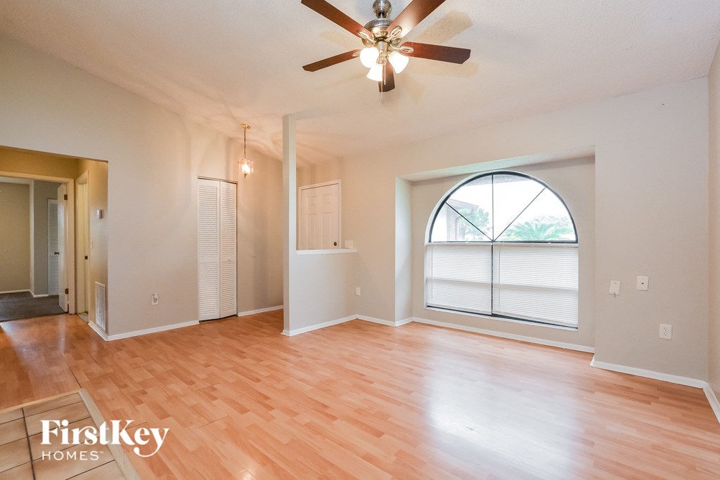 an empty living room with a large window and a ceiling fan