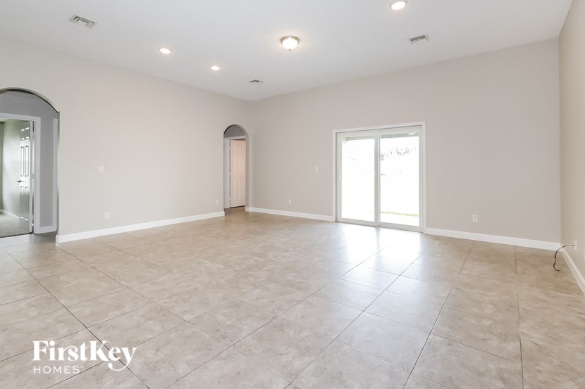 an empty living room with tile flooring and a door to the kitchen