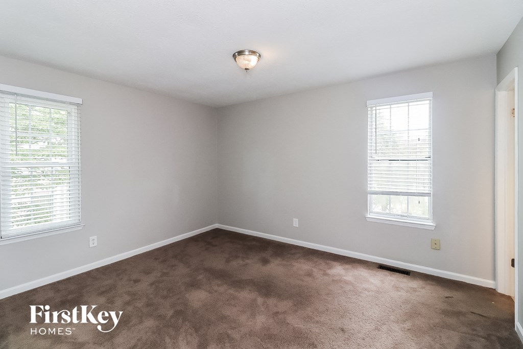 A room with a carpeted floor and two windows.