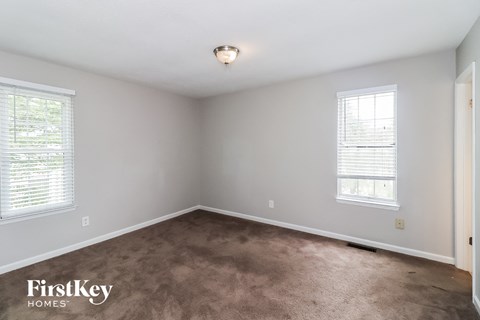 A room with a carpeted floor and two windows.