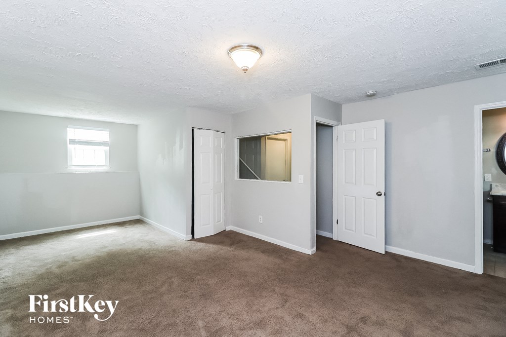 A room with a carpeted floor and white walls, with a window on the left wall.