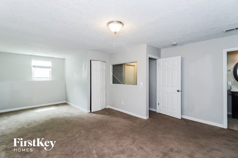 A room with a carpeted floor and white walls, with a window on the left wall.